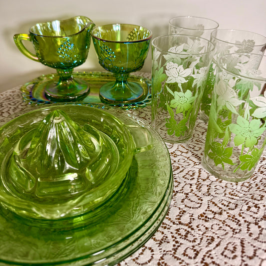 Vintage green uranium‑glass juicer with matching cream & sugar and floral‑engraved tumblers on lace cloth.